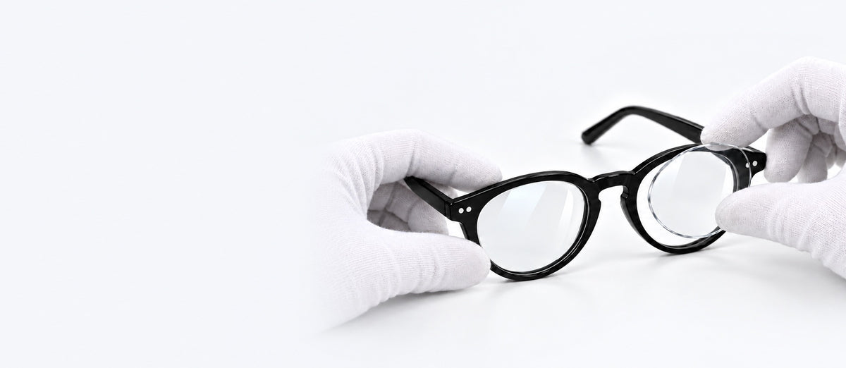 Nye glas monteres i et sort brillestel af hænder med hvide optikerhandsker.